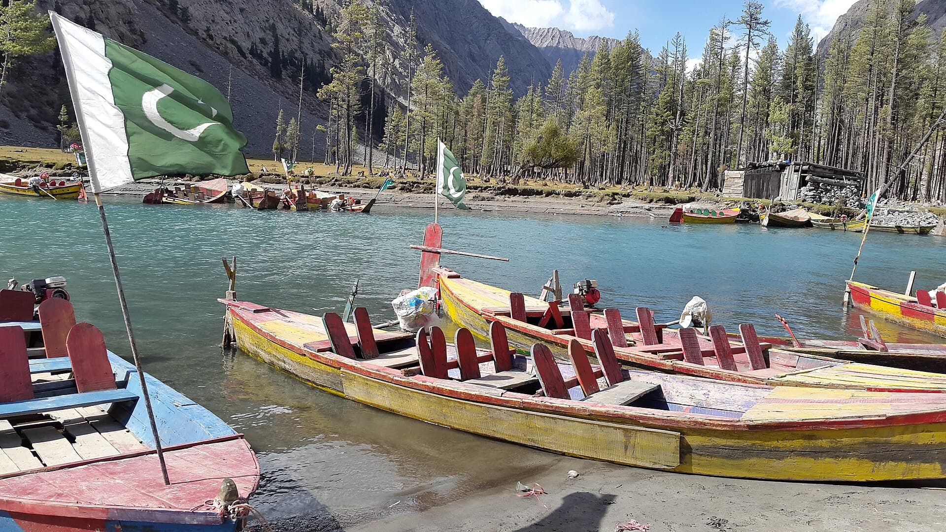 Colourful boats on Mahodand Lake beneath pine-covered mountains